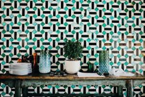 Vases et assiettes sur un meuble en bois devant un mur en mosaique verte, blanche et noire